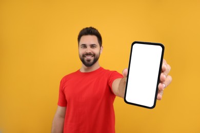 Young man showing smartphone in hand on yellow background, selective focus. Mockup for design