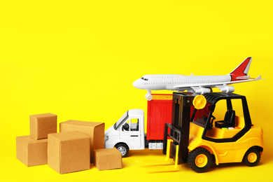 Photo of Different toy vehicles with boxes on yellow background. Logistics and wholesale concept