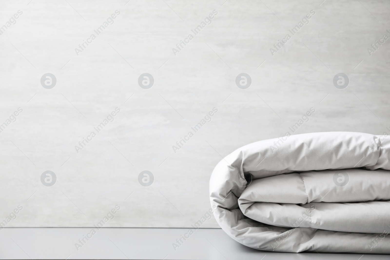 Photo of Soft folded blanket on light grey table, closeup. Space for text