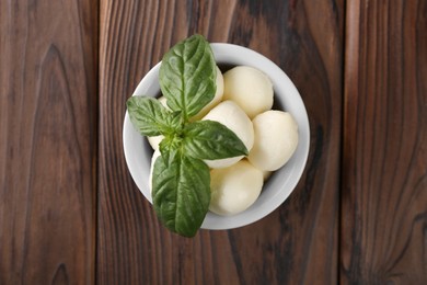 Photo of Tasty mozarella balls and basil leaves in bowl on wooden table, top view