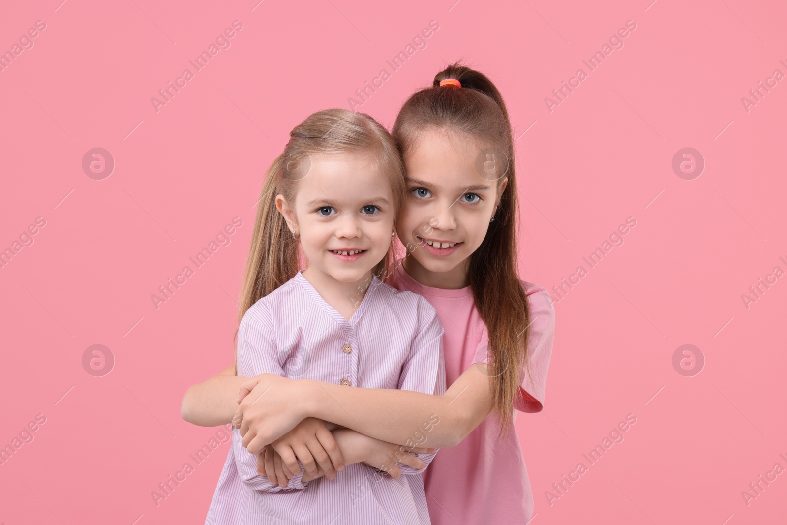 Photo of Portrait of cute little sisters on pink background