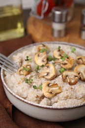 Photo of Delicious barley porridge with mushrooms and microgreens in bowl on table, closeup