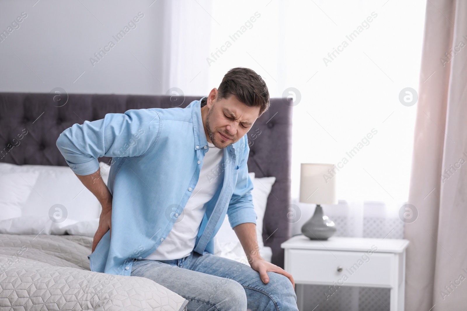 Photo of Young man suffering from back pain at home