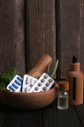 Photo of Mortar with fresh green herbs, extracts and pills on wooden table