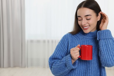 Happy young woman holding red ceramic mug at home, space for text