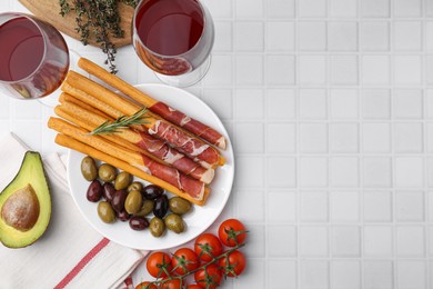 Delicious grissini sticks with prosciutto and ingredients on white table, flat lay. Space for text