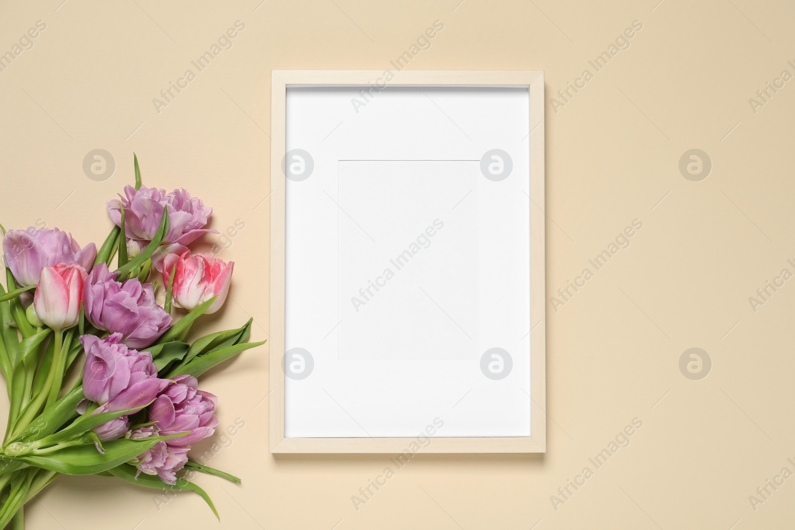 Photo of Empty photo frame and beautiful tulip flowers on beige background, flat lay. Space for design