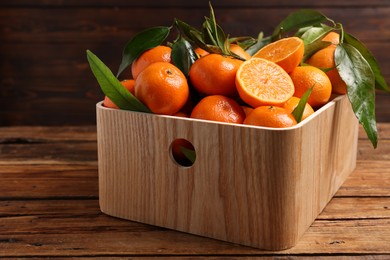 Fresh tangerines with green leaves in crate on wooden table