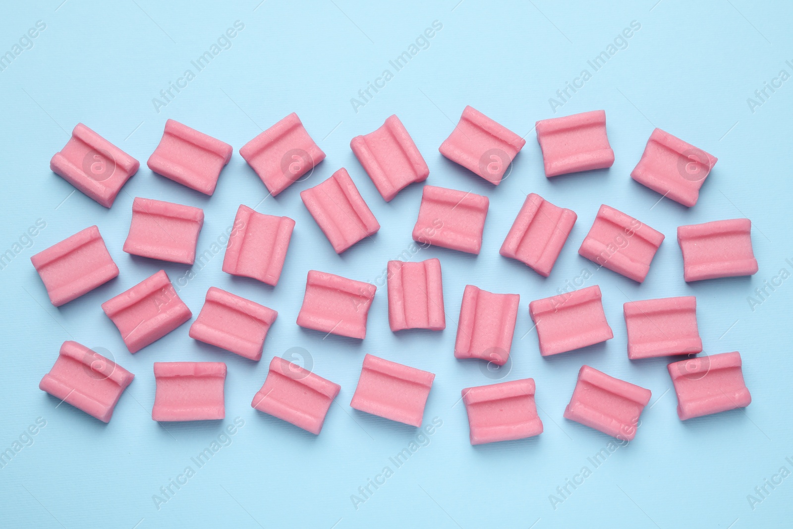 Photo of Tasty pink chewing gums on light blue background, flat lay