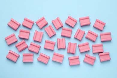 Photo of Tasty pink chewing gums on light blue background, flat lay