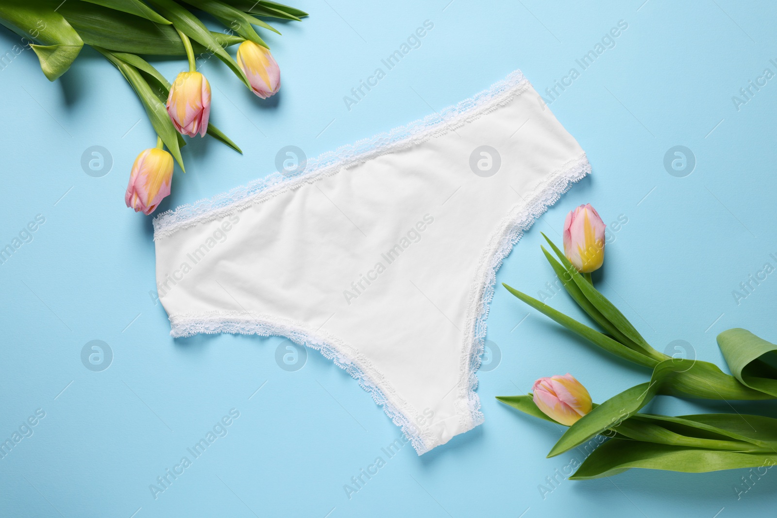 Photo of Comfortable white women's underwear and beautiful tulips on light blue background, flat lay