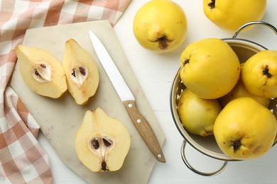 Photo of Tasty ripe quinces, metal colander and knife on white wooden table, flat lay