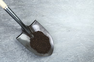 Photo of Metal shovel with fertile soil on gray textured surface, top view. Space for text