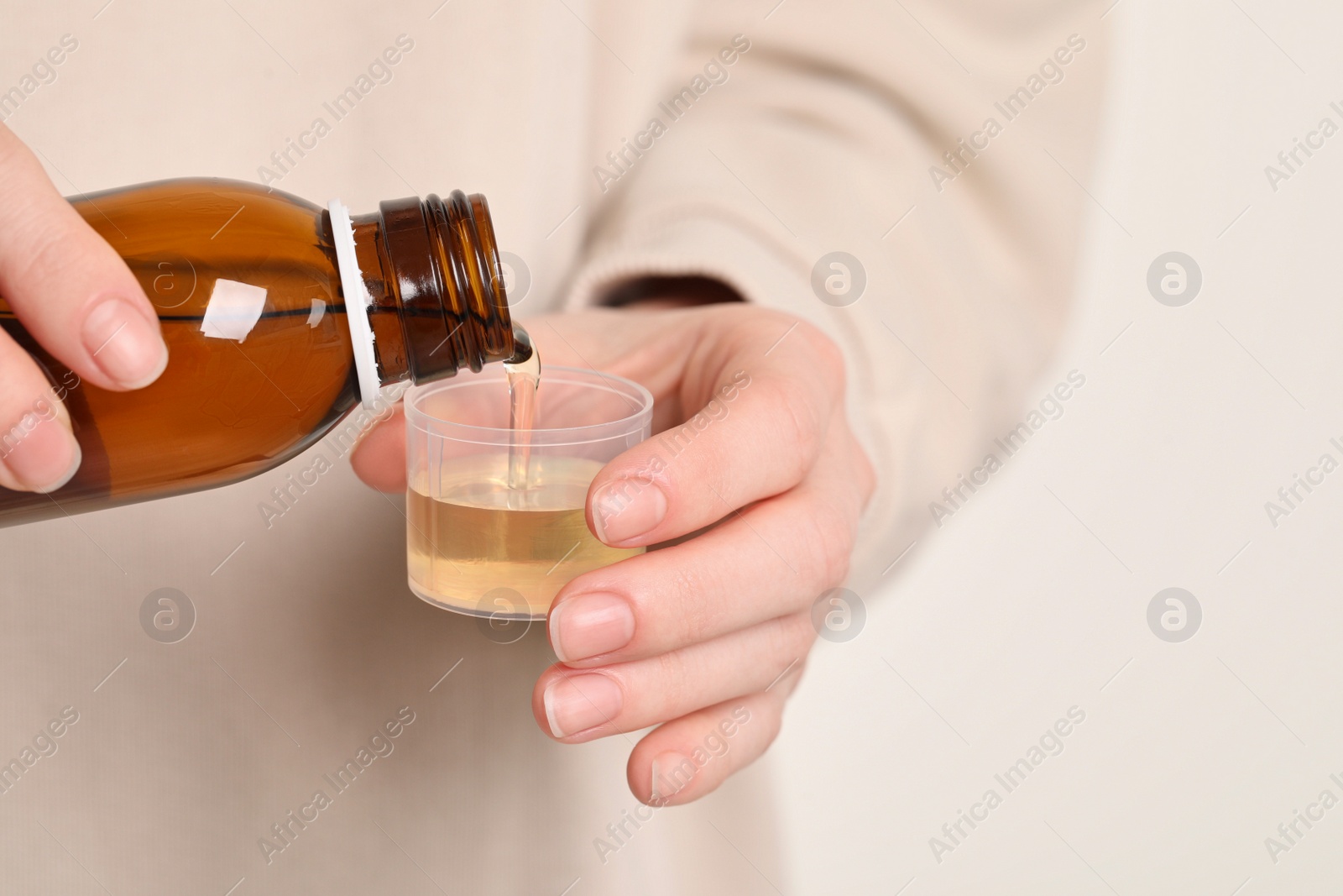 Photo of Woman pouring syrup from bottle into measuring cup, closeup. Cold medicine