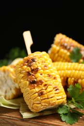 Photo of Tasty grilled corn cobs on wooden board, closeup