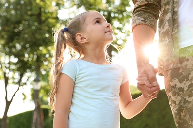 Photo of Father in military uniform walking with his daughter at sunny park