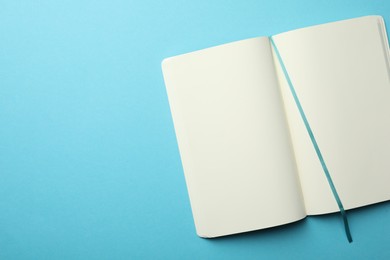 Stylish open notebook with blank sheets on light blue background, top view. Space for text