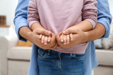 Photo of Father holding hands with his child indoors, closeup. Happy family