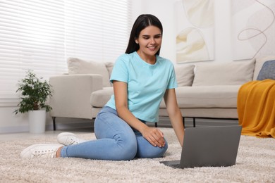 Photo of Happy young woman having video chat via laptop on floor in living room