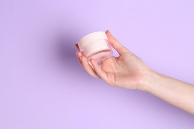 Woman holding jar of cream on violet background, closeup. Space for text