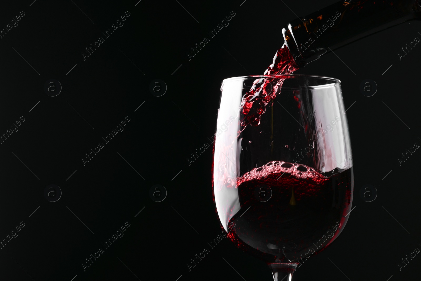 Photo of Pouring red wine into glass against black background, closeup. Space for text