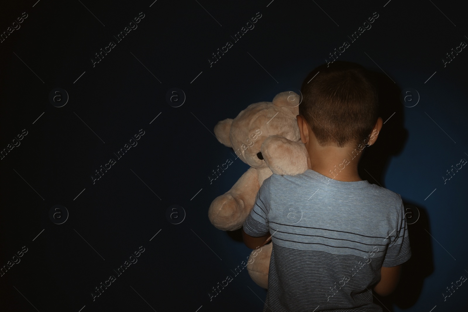 Photo of Little boy with teddy bear near blue wall, back view and space for text. Domestic violence concept