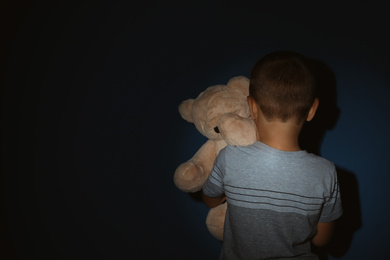 Photo of Little boy with teddy bear near blue wall, back view and space for text. Domestic violence concept