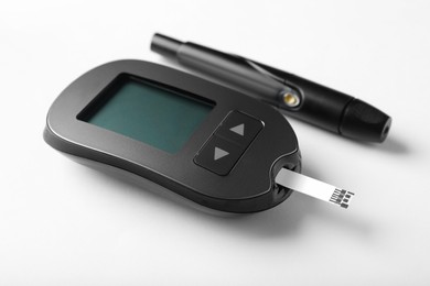 Digital glucometer with test strip and lancet pen on white background. Diabetes control