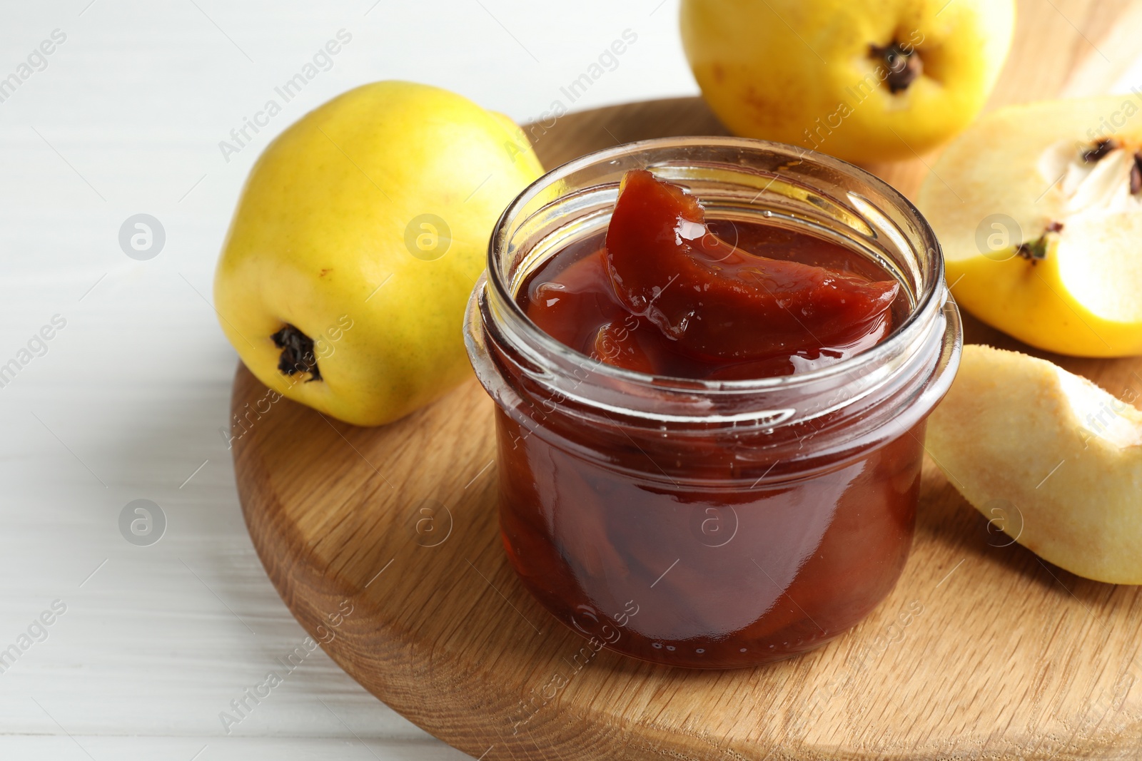 Photo of Tasty homemade quince jam in jar and fruits on white wooden table, closeup