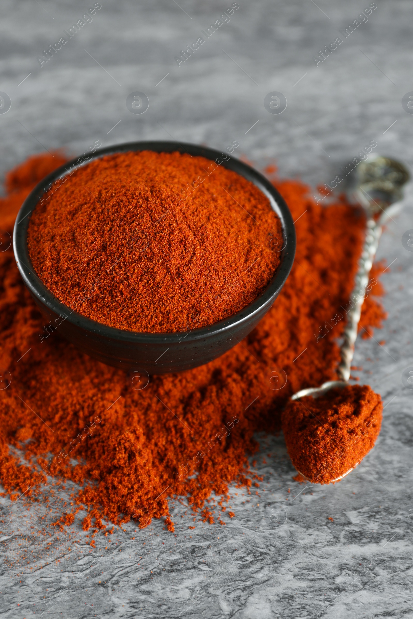 Photo of Bowl, spoon and paprika on grey marble table, closeup