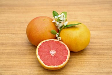 Photo of Fresh ripe grapefruits, flowers and green leaves on wooden table