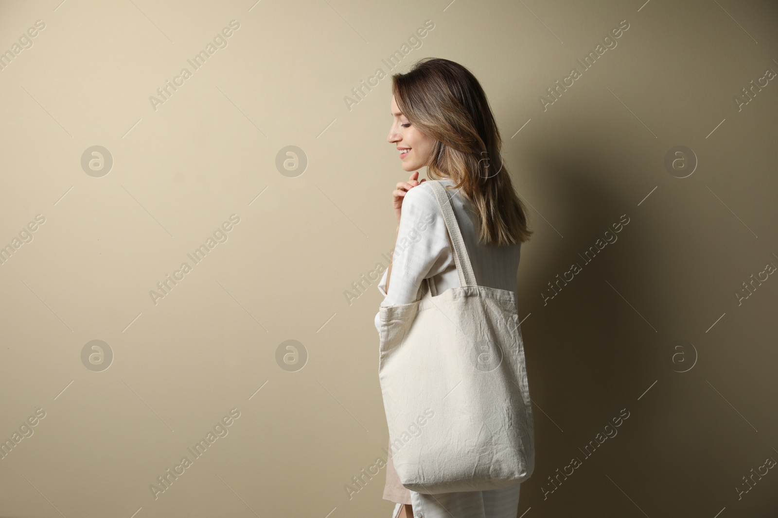 Photo of Happy young woman with blank eco friendly bag against beige background. Space for text