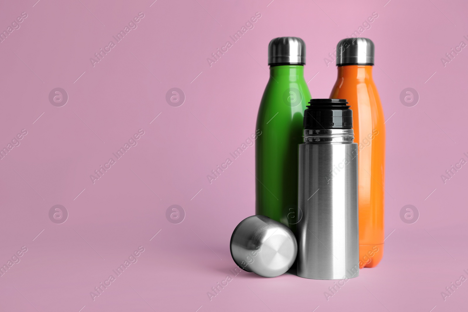 Photo of Stylish thermo bottles on pink background, space for text