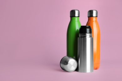 Stylish thermo bottles on pink background, space for text