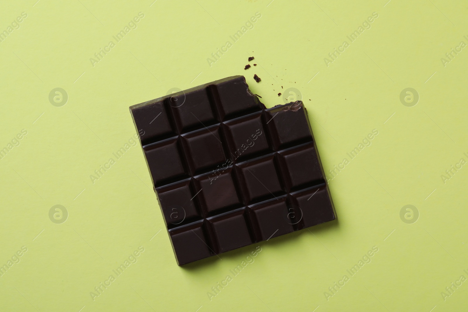 Photo of Tasty dark chocolate bar with bite mark on yellow background, top view