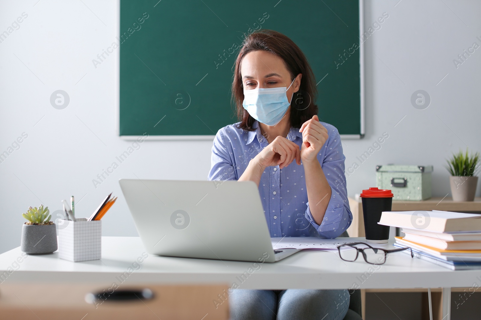 Photo of Teacher with protective mask conducting online lesson in classroom during COVID-19 quarantine