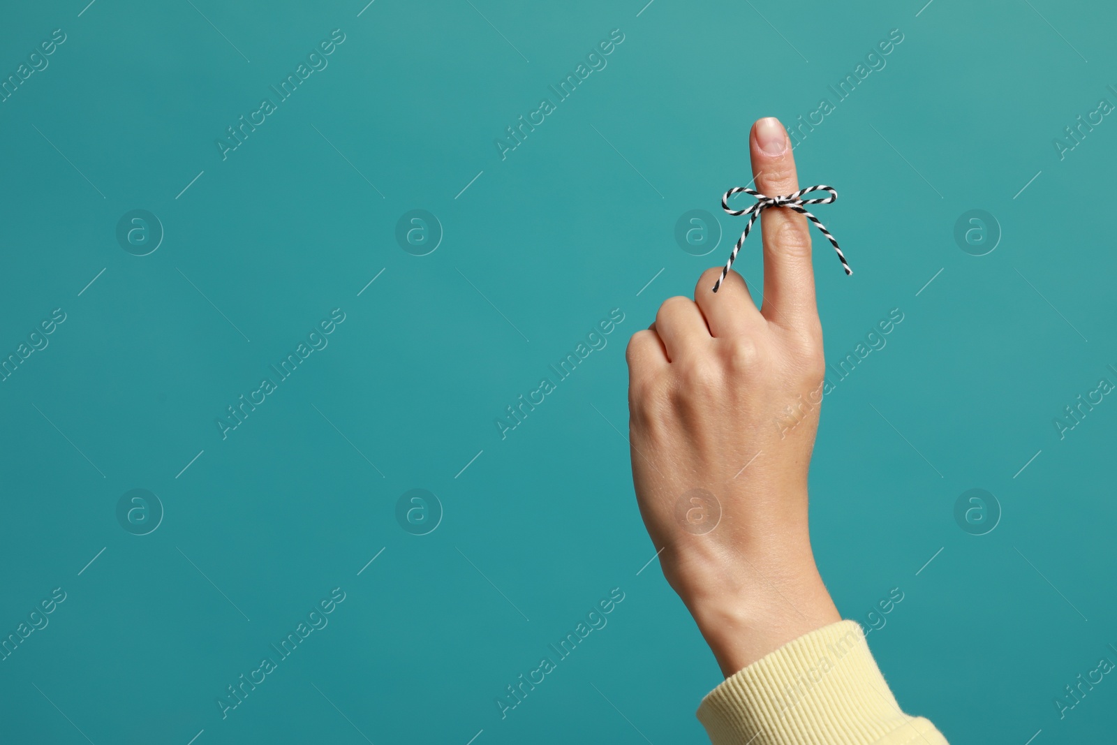 Photo of Woman showing index finger with tied bow as reminder on light blue background, closeup. Space for text