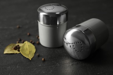 Salt and pepper shakers with bay leaves on black table, closeup
