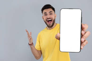 Image of Happy man holding smartphone with empty screen on grey background, space for text