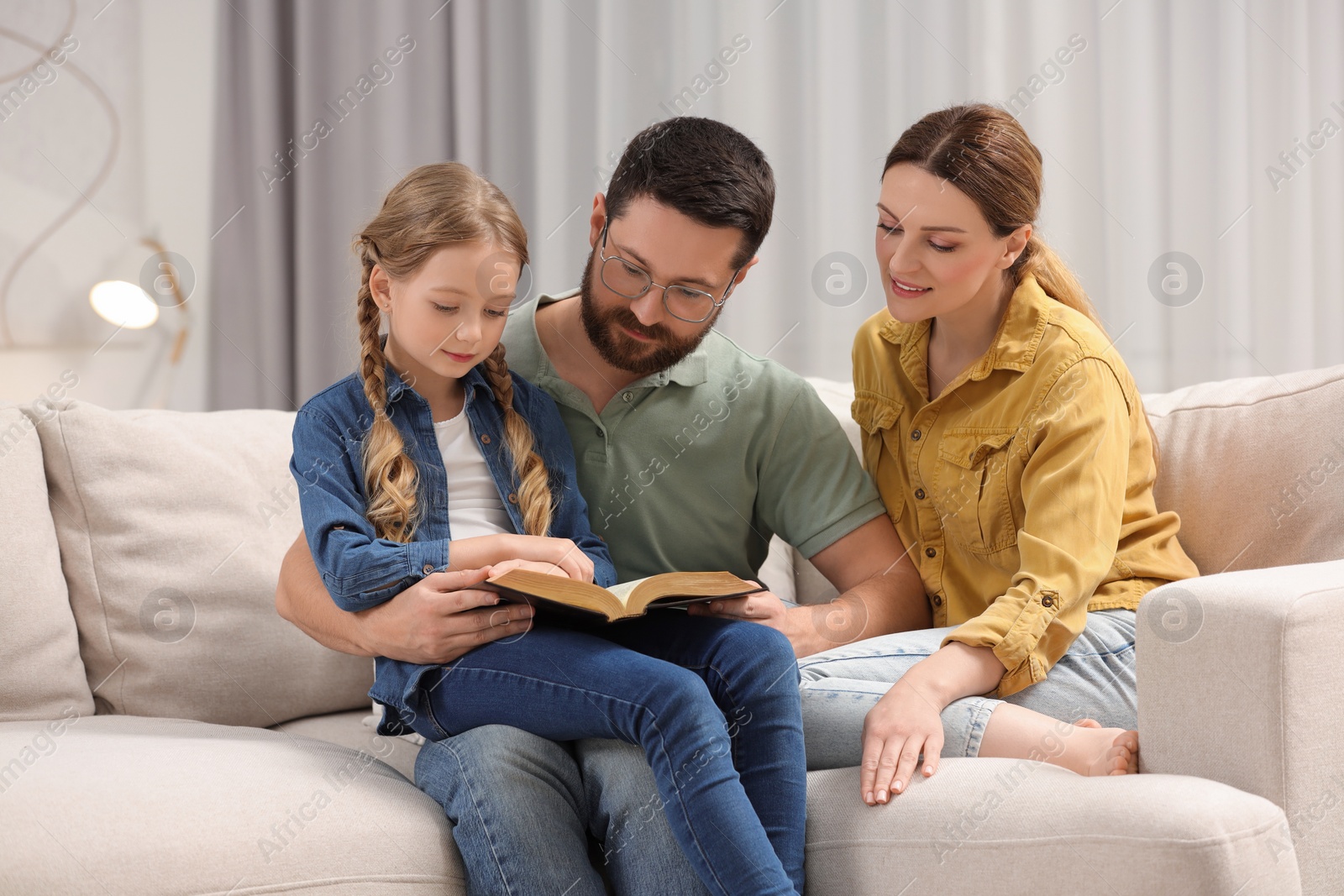 Photo of Girl and her godparents reading Bible together on sofa at home