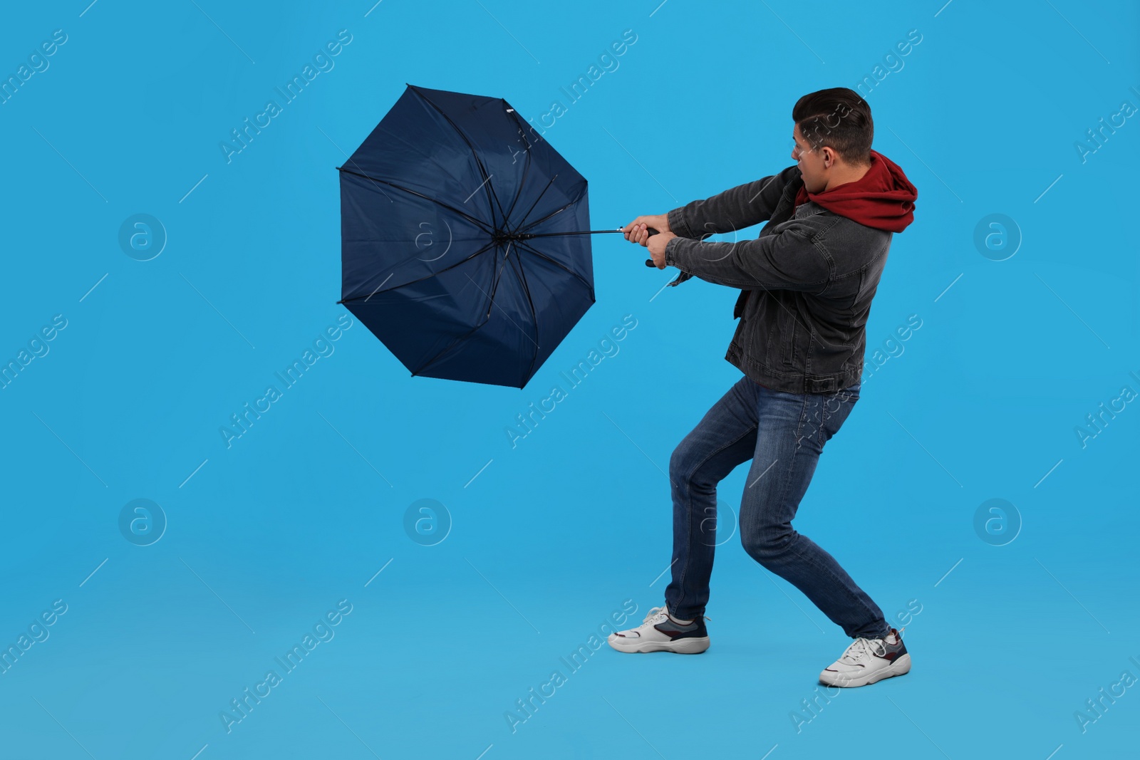 Photo of Man with umbrella caught in gust of wind on light blue background