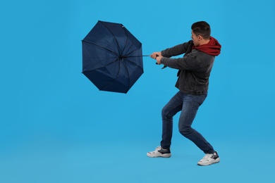 Photo of Man with umbrella caught in gust of wind on light blue background