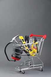 Photo of Small shopping cart with set of construction tools and headphones on grey background