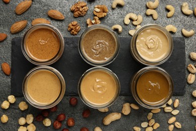 Photo of Tasty nut butters in jars and raw nuts on gray table, flat lay