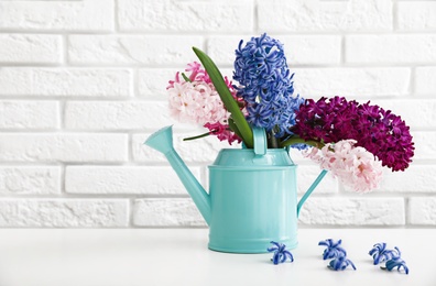 Photo of Beautiful hyacinths in watering can on table against brick wall, space for text. Spring flowers