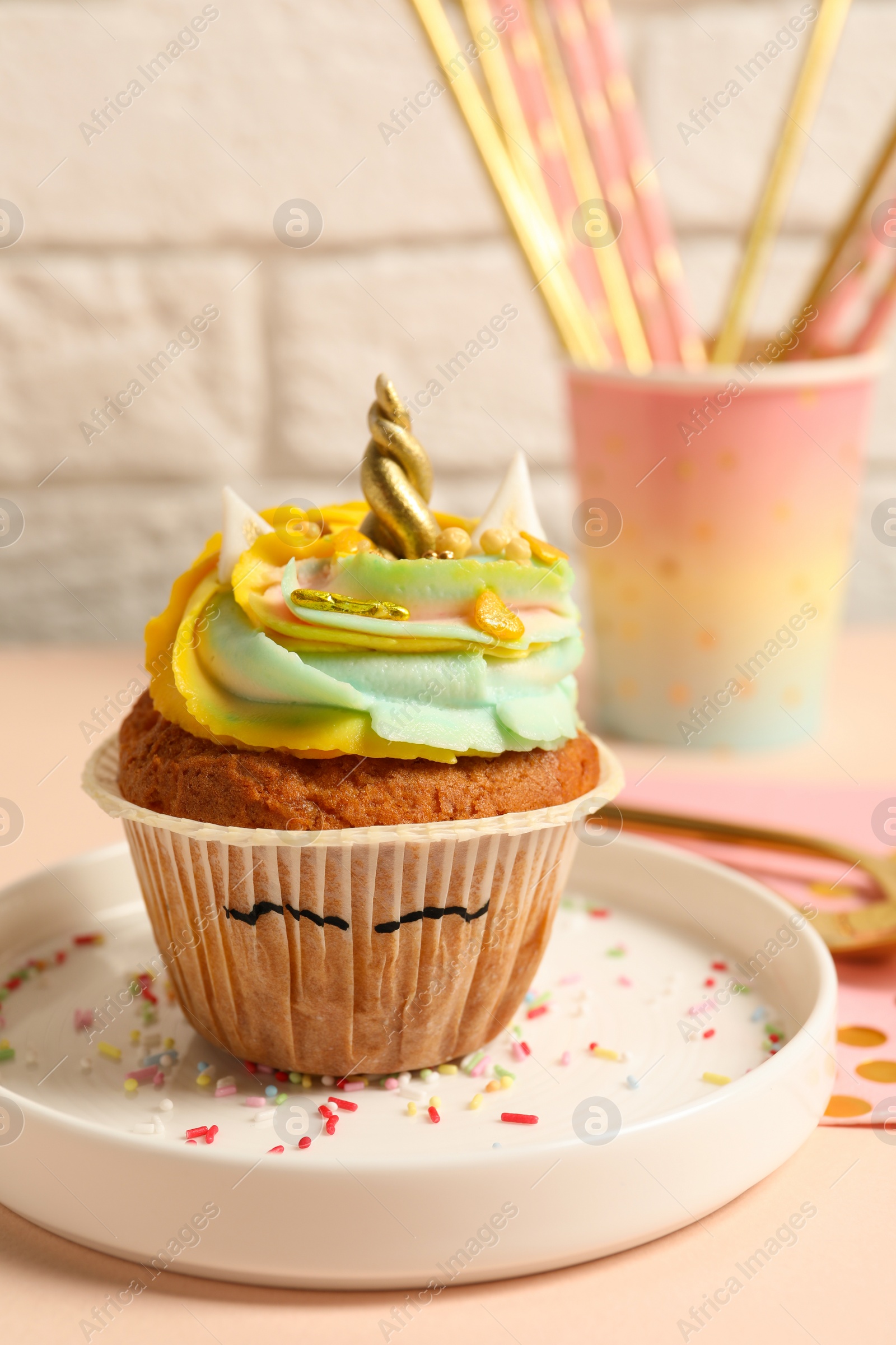 Photo of Plate with cute sweet unicorn cupcake on beige table