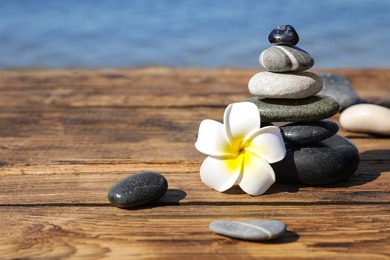 Photo of Stack of stones and flower on wooden pier near sea, space for text. Zen concept