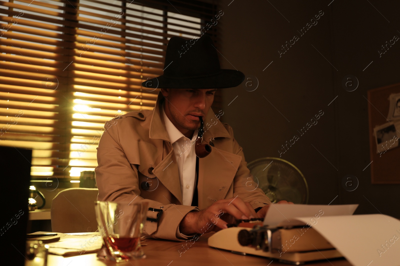 Photo of Old fashioned detective with smoking pipe using typewriter at table in office