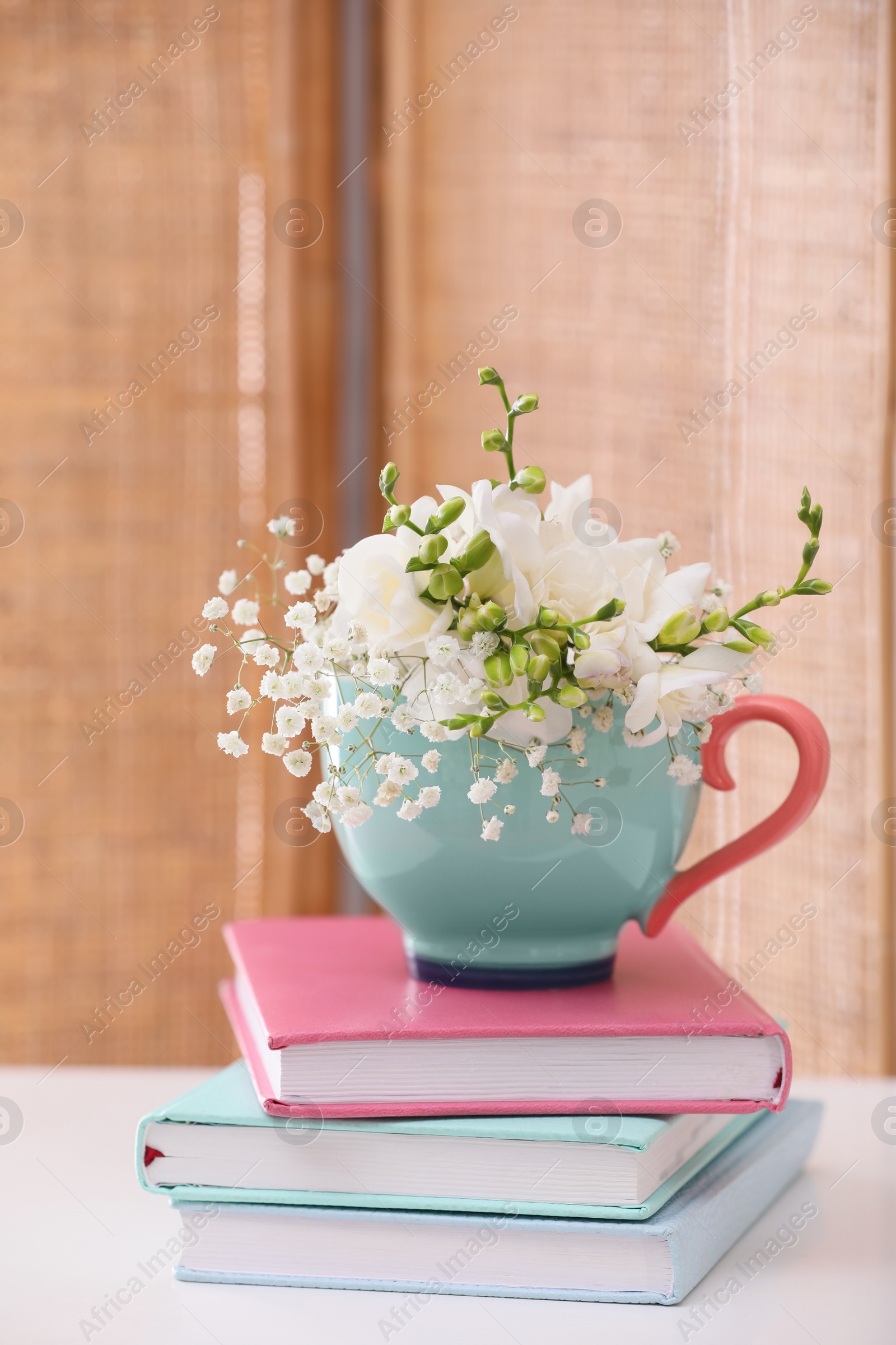 Photo of Beautiful bright flowers in cup and books on white table indoors