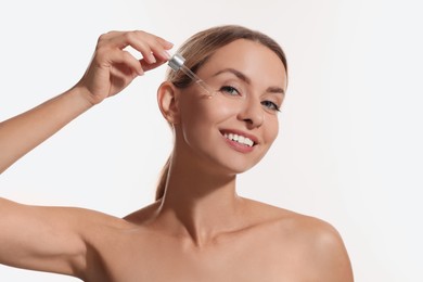 Beautiful woman applying cosmetic serum onto her face on white background